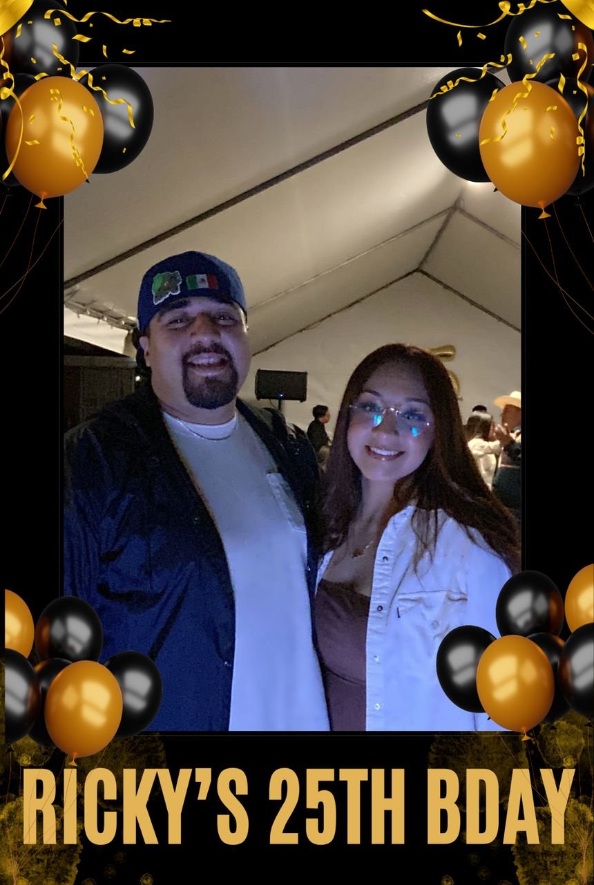 A couple posing with a gold and black balloon backdrop at a birthday photo booth