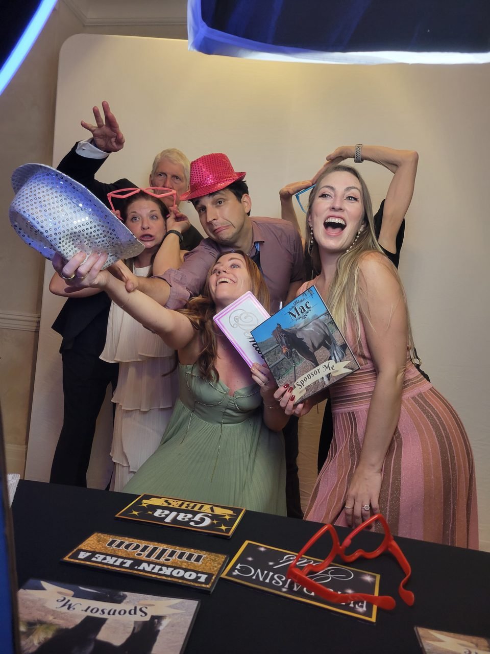Guests in formal dress laughing with hats and novelty glasses at a SoCalFun365 photo booth during a charity gala in Orange County