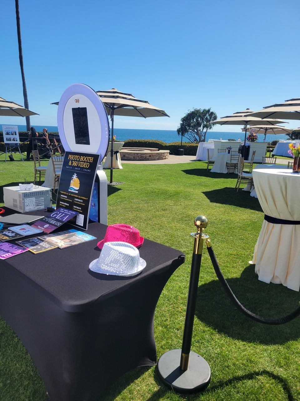 A SoCalFun365 photo booth with velvet stanchions on an oceanfront lawn at an Orange County charity gala